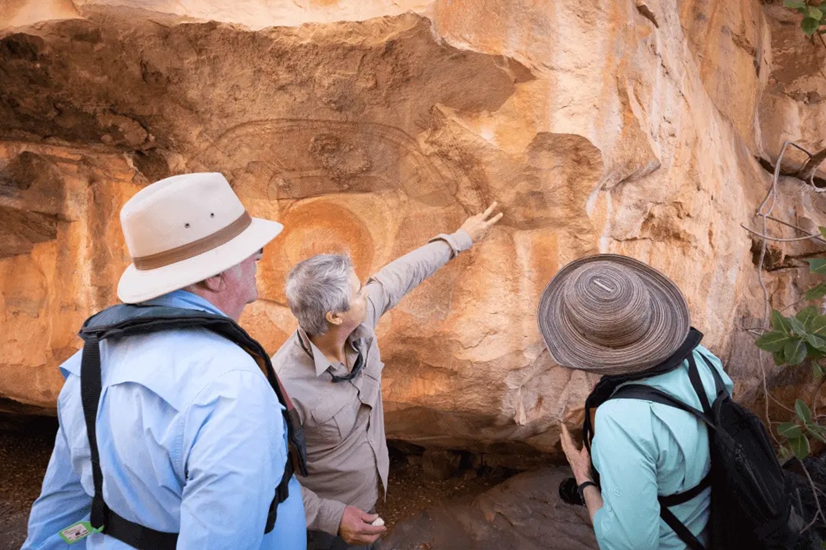 Photo of three people looking up at a large orange rock in the Kimberley