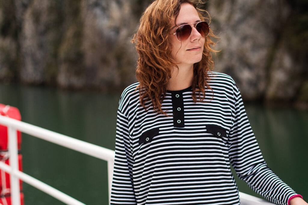 A brown-haired woman in a striped shirt stands holding the white rail on a boat