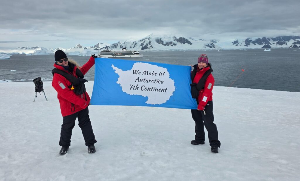 Kerry and Michelle holding up a sign on their Antarctica Cruise with Viking